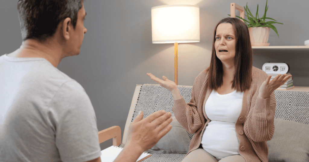 A distressed pregnant woman gesturing helplessly during a counseling session, illustrating how a narcissist's cruelty during pregnancy is one of the most self-destructive choices that ultimately exposes and destroys them.