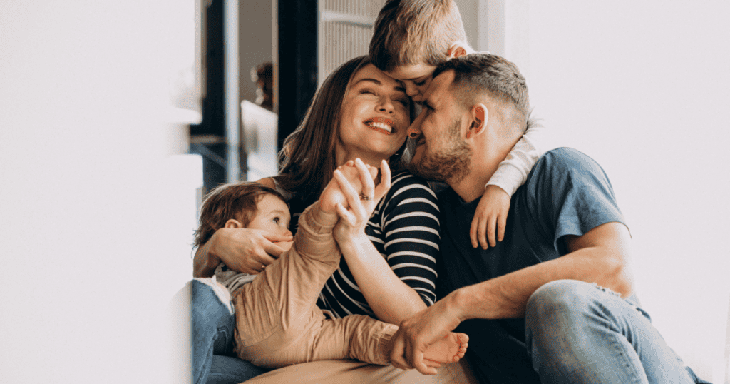 A glowing couple cuddled with their children in a warm, joyful home — the exact kind of genuine love and peace a narcissist cannot stand knowing their ex built without them.