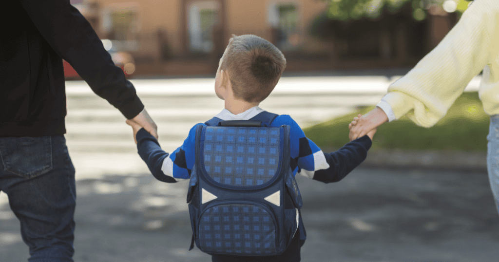 A young child holding both parents' hands on the way to school, representing the public, child-focused setting where a narcissist can't control the spotlight or the narrative.