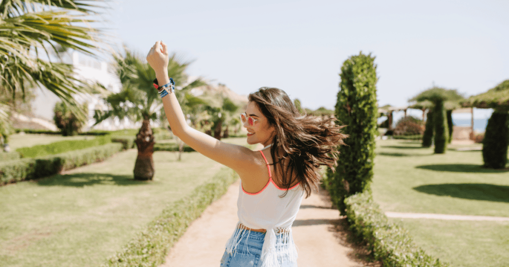 A woman striding freely through a sunlit garden with her arm raised in joy, reminding you that being a narcissist's defeat means you were powerful enough to threaten them.