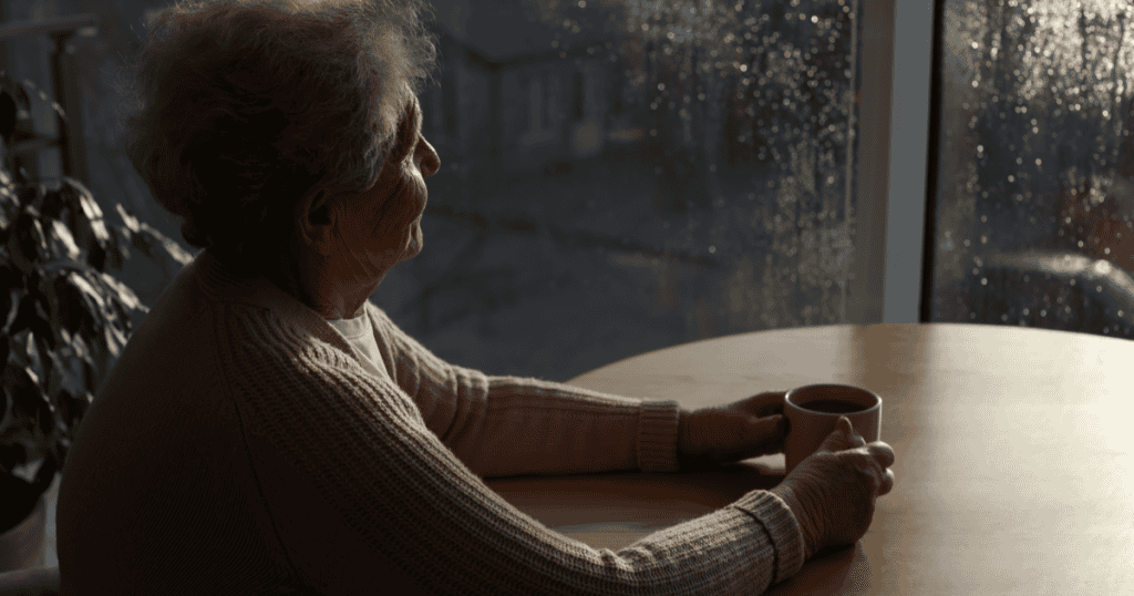 An elderly person sitting alone in the dim light of a rainy window, embodying the ultimate defeat a narcissist faces when age strips away their power, charm, and the audience they depended on.