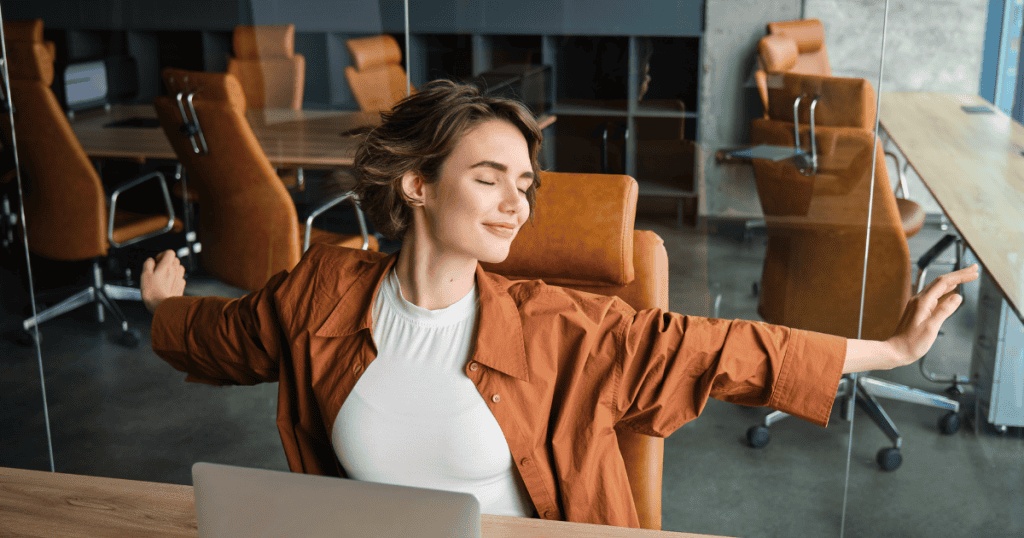 A woman leans back and stretches contentedly at her office desk with her eyes closed, demonstrating that another person's unease is often a sign of your own unshakeable peace and self-assurance.