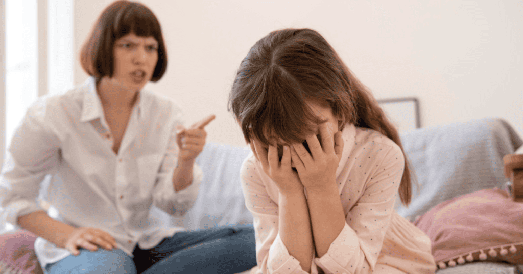A young girl covering her face in tears while a mother points and scolds her, depicting the childhood environment of fear and shame that many narcissistic abuse survivors grew up in without realizing it was abnormal.