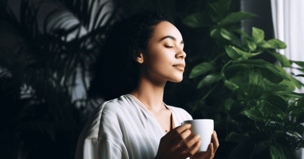 A woman peacefully inhales the aroma of a warm mug surrounded by lush green houseplants, capturing the quiet, restorative calm of reclaiming your own rhythm.