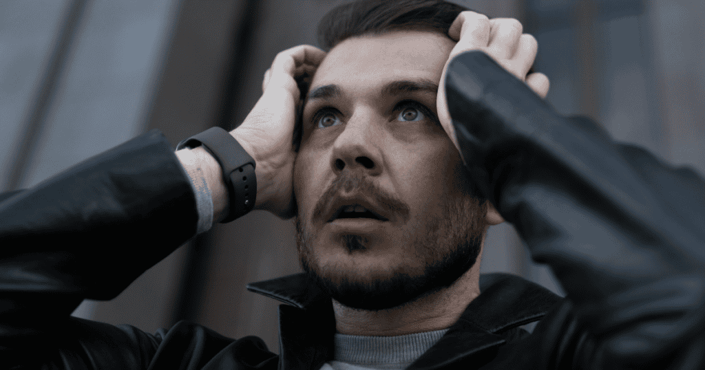 A man in a leather jacket clutches his head and stares upward in shock, capturing the stunned panic a narcissist feels when their carefully built image is suddenly exposed.