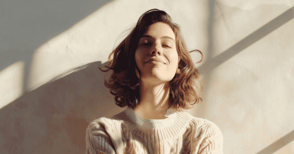 A woman with chin-length curls tilts her head back with a serene, confident smile in diagonal sunlight, embodying the peaceful certainty that comes with validating your own reality.