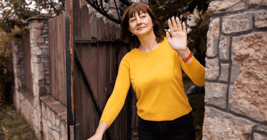 A woman waves goodbye while stepping through a gate with a faint, apologetic smile, reflecting the brush-off of "I forgot and double-booked."