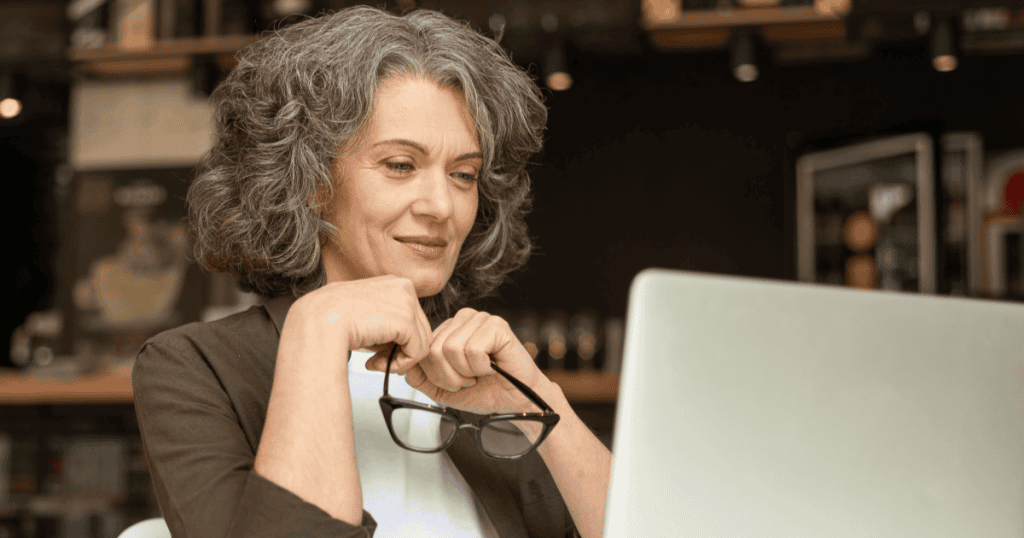 A woman smiles at her laptop screen while holding her glasses, illustrating the "working late" excuse used to avoid making time for a partner.
