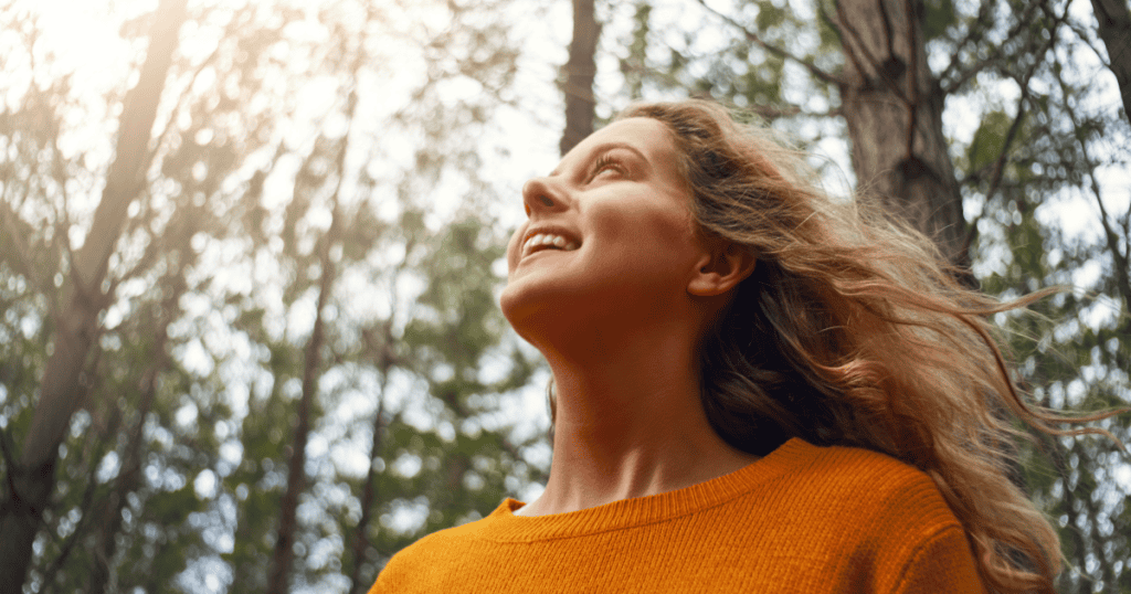 A woman smiling freely beneath sunlit trees, reminding you that recognizing the signs of a narcissistic upbringing isn't the end of your story — it's where healing begins.