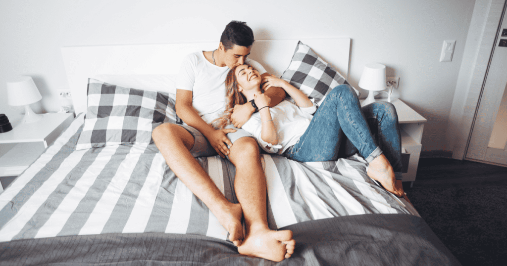 A couple laughing and cuddling freely in bed, representing the genuine intimacy that becomes possible once you've broken free from a narcissist's hidden bedroom control.