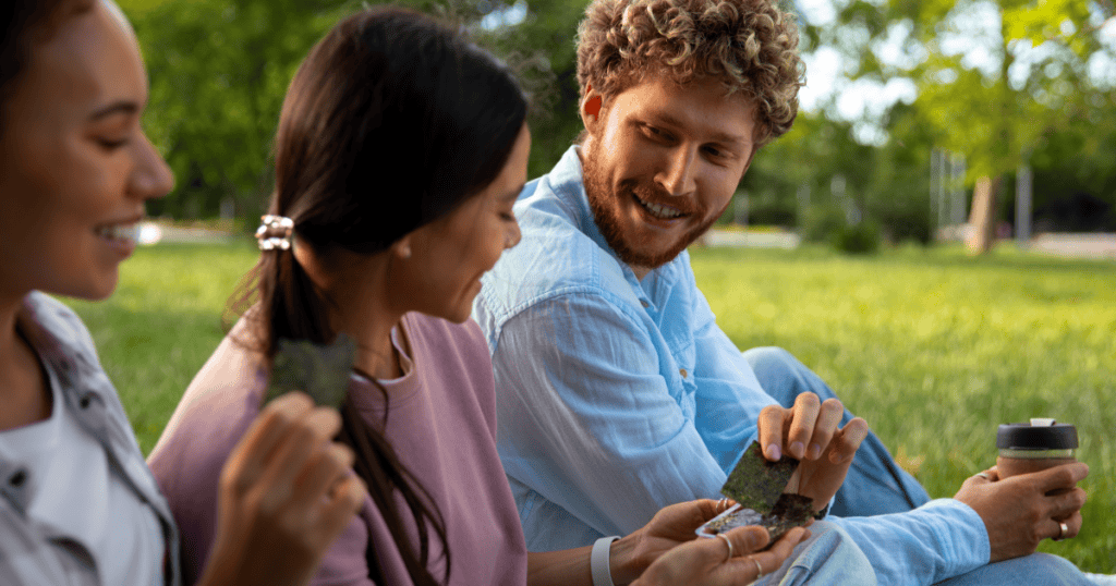 A charming man engaging casually with women in a sunny park, illustrating how narcissists use relaxed public spaces to identify and approach their next target under the guise of friendly conversation.