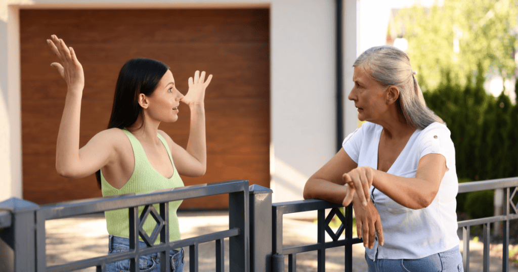 A woman raises her hands animatedly while talking to another woman across a gate, capturing the empty promise of "we can rearrange for another time."