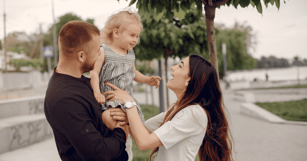 A man holds a delighted toddler while a laughing woman reaches for her, capturing a warm family moment that shows what genuine time together could have looked like.