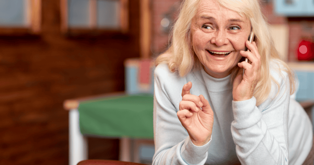 An older woman laughs eagerly into her phone with an animated, ingratiating expression, illustrating how a narcissist's flattering deference is really aimed at the money and status a person represents, not the person themselves.