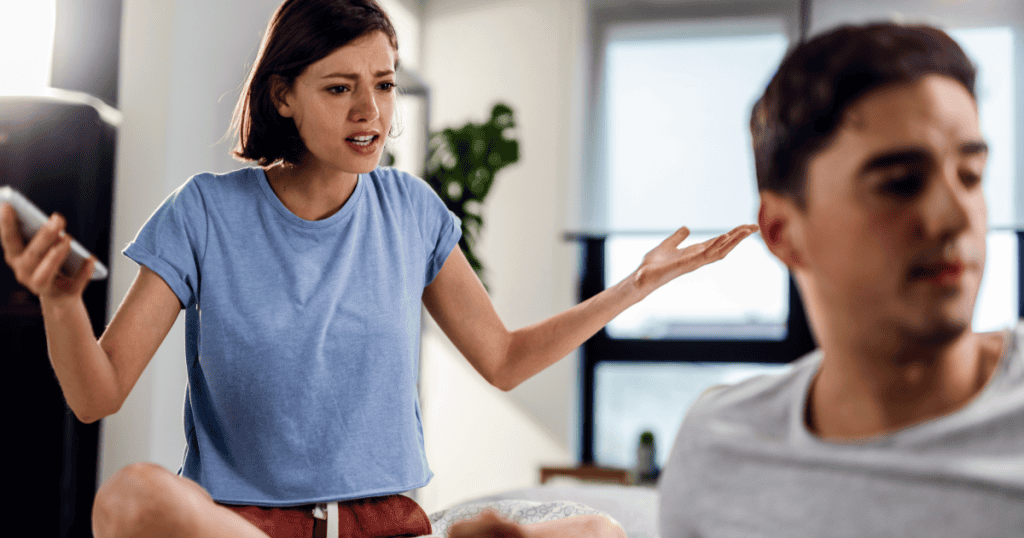 A woman gestures with an exasperated expression while holding her phone as a man beside her looks away, capturing the real message hidden behind the constant comparisons.