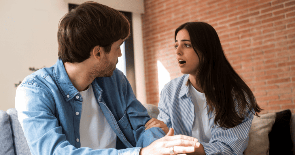 A woman speaks earnestly while touching a man's arm on the couch, reflecting how focusing on the ex can distract from examining his own behavior.