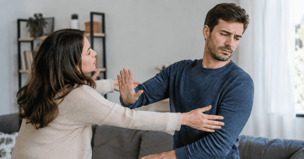 A man holds his hand up to keep a woman at a distance as she reaches toward him, capturing the emotional withdrawal behind struggles with intimacy that reflect on him, not her.