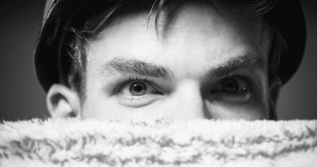 A man peers over a fluffy collar with only his watchful eyes showing, symbolizing how a covert narcissist hides behind a quiet exterior while their subtle habits give them away.