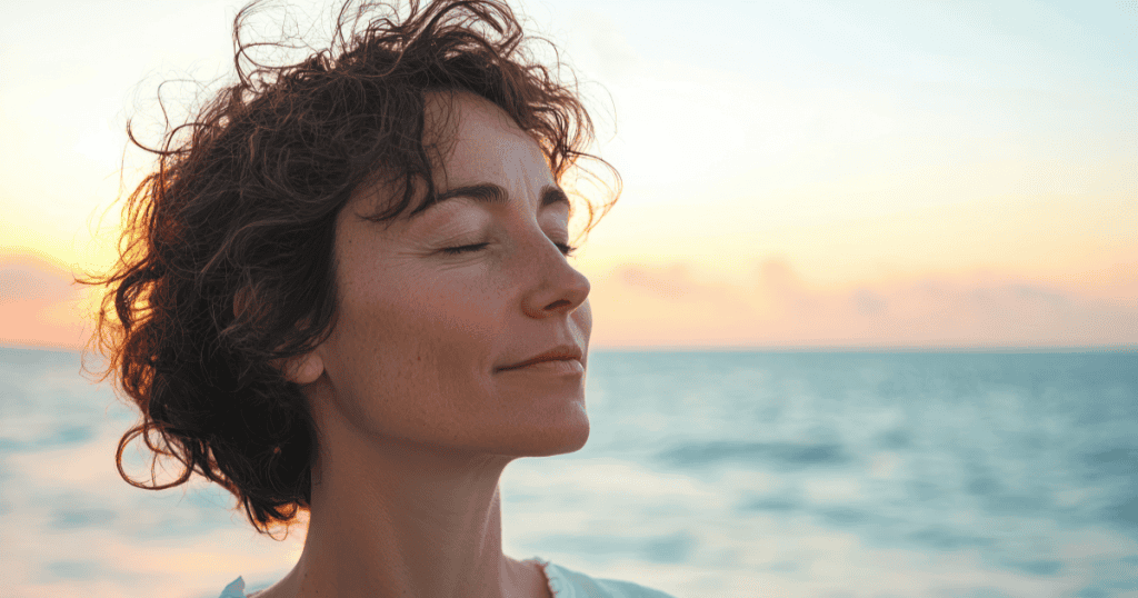 A woman closes her eyes and breathes in the ocean breeze at sunset with a peaceful expression, reflecting the calm clarity of recognizing that a covert narcissist’s small habits all point to the same truth.