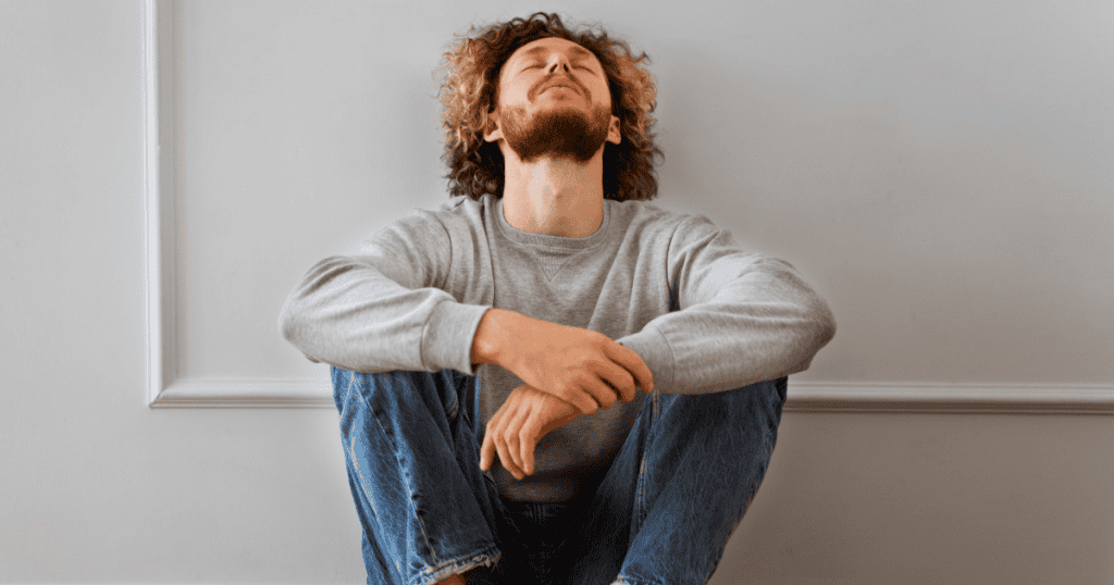A man sits against a wall with his head tilted back and eyes closed in restless frustration, capturing how a narcissist stays haunted by a super empath they can never fully move on from.