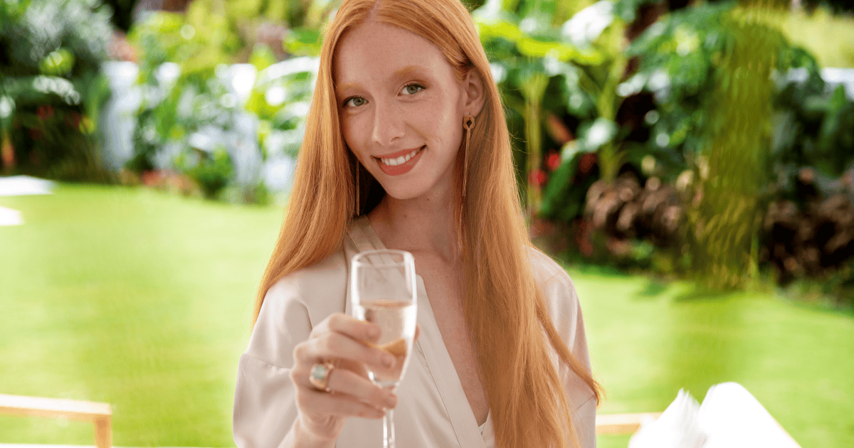 A confident red-haired woman smiles warmly and raises a glass of champagne in a lush garden, celebrating the realization that a narcissist's treatment of you reflected their values, not your worth.
